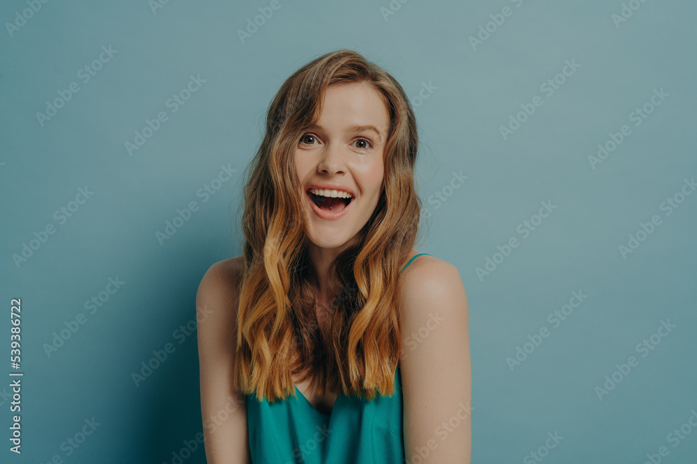 Fototapeta premium Excited young woman showing on camera positive surprised facial expression and broadly toothy smile