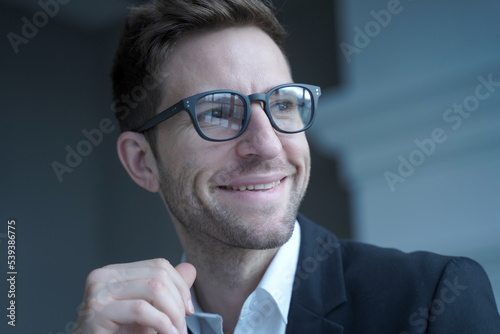 Positive young male entrepreneur in glasses and formal wear looking aside with pleasant smile