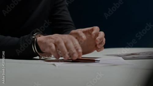Suspected criminal in handcuffs signs papers with confession of his guilt. Interrogation. Police officer detective forced killer to confess to crime. FBI agent asks to sign documents. Law and justice