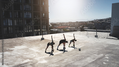 Fitness group  stretching and ball sports with friends doing exercise  workout and warm up on city building rooftop on a summer day. Athlete man and women during soccer training or football practice