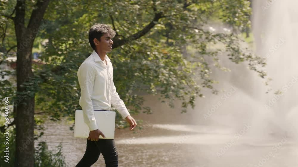 Tracking shot of man walking at park carrying a laptop for online remote work Tracking shot of man walking at park carrying a laptop for online remote work