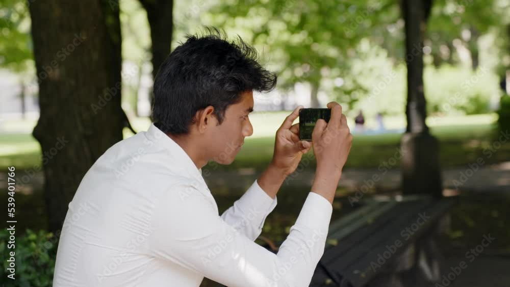 Rear side closeup of Indian man taking pictures of park with smartphone Rear side closeup of Indian man taking pictures of park with smartphone