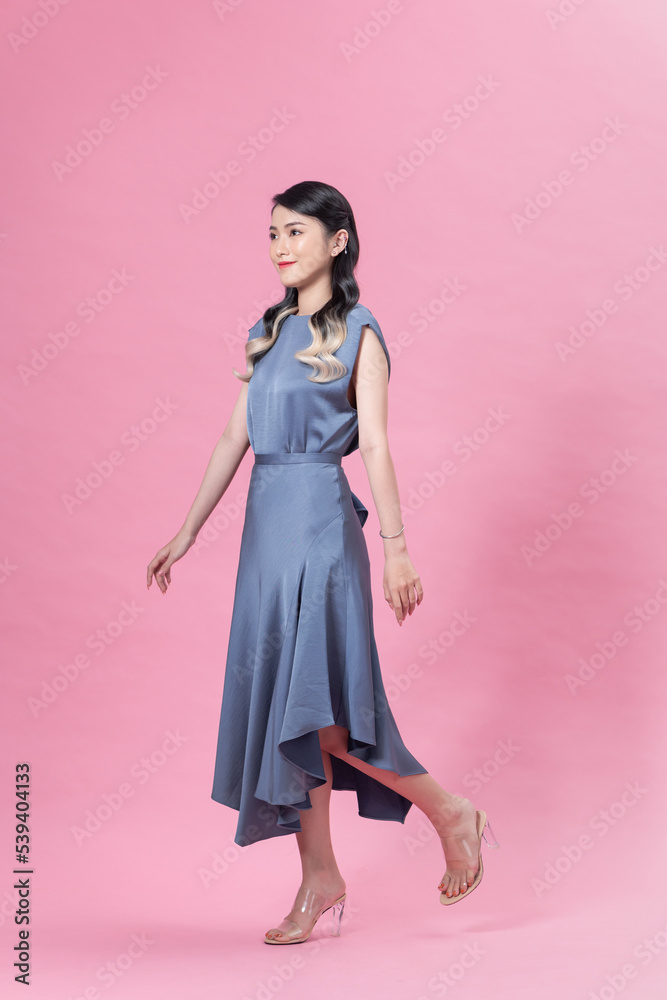 Pretty young female model in dress walking on pink background and smiling