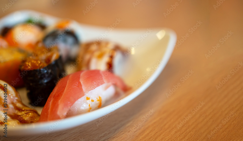 Various sushi in a white plate placed on a wooden table