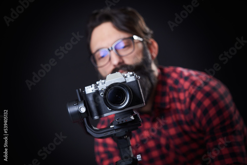 Video recording with a gimbal; bearded man, content creator, maneuvering his mirrorless camera while recording footage