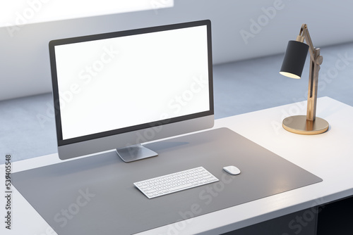 Close up of office desk top with empty white computer monitor and mock up place for your advertisement, lamp and keyboard on blurry background. 3D Rendering.