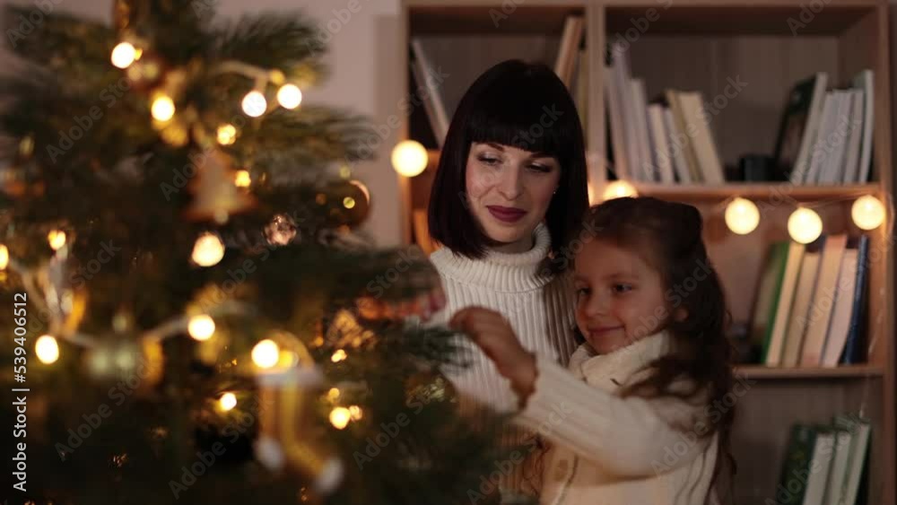 Happy small preschool caucasian child girl decorating Christmas tree with happy young mother, putting toys on branches, enjoying preparing for New Year celebration at home, miracle time concept. Happy small preschool caucasian child girl decorating Christmas tree with happy young mother, putting toys on branches, enjoying preparing for New Year celebration at home, miracle time concept.