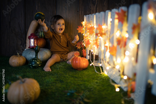 Cute small baby is staying near a lot of pumpkins in at autumn and halloween decorated scenography. Studio photography.