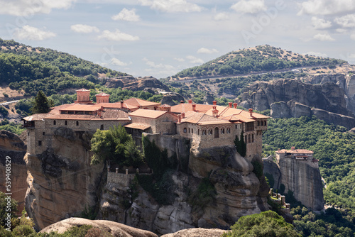 Panoramic view of two neighboring Meteora Monasteries - St. Varlaam and Rousanou among wooded hills and valleys in region of Thessaly, Kalampaka, Greece