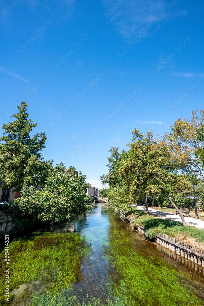 Water canal, green trees and blue skies. L'Isle-sur-la-Sorgue in summer. South of France