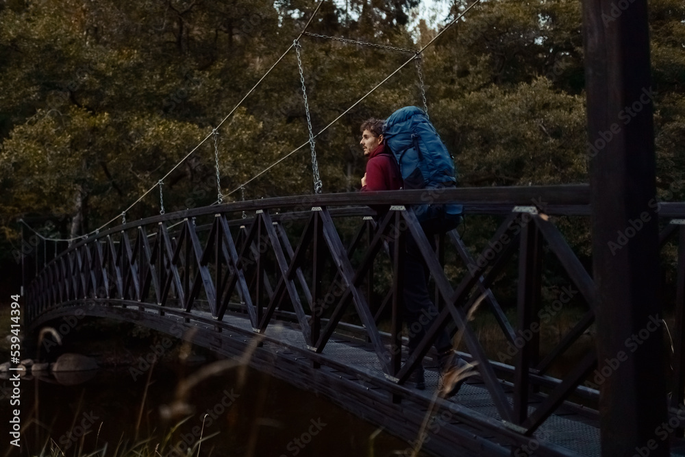 A caucasian man with a backpack walking on a bridge in the forest. A caucasian man with a backpack walking on a bridge in the forest.