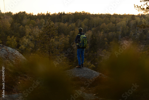 A man with a backpack standing on a rock in the forest at sunset.