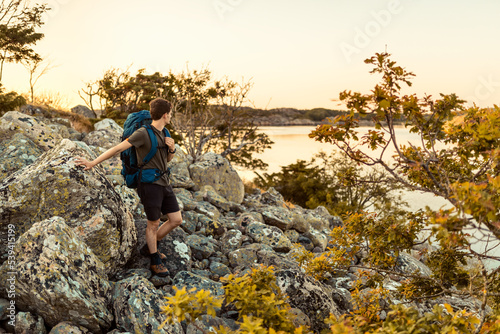 A caucasian man hiking by the sea with a backpack at sunset. © Francis