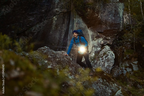 A caucasian man hiking in the forest with a flashlight and a backpack.