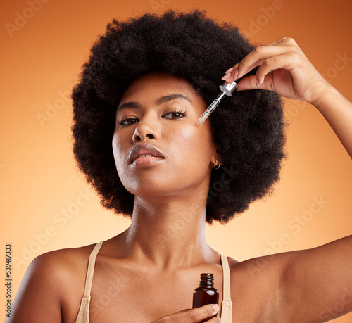 Black woman beauty, facial serum and essential oil for glowing, healthy and aesthetic skincare on orange studio background. Portrait young african model liquid cosmetics bottle product for clean face