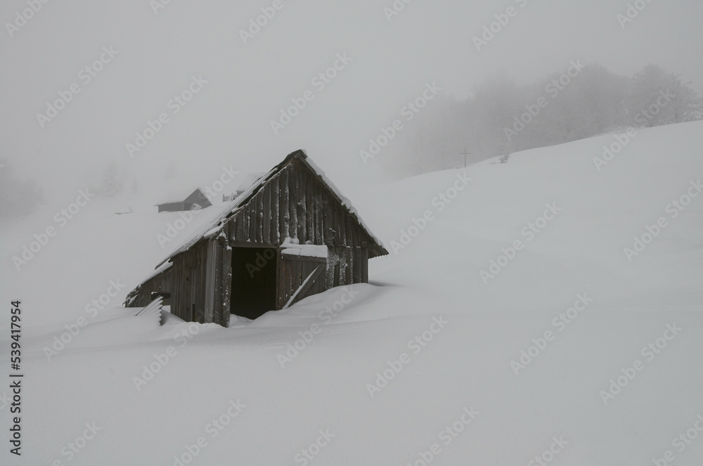 Abandoned hut covered in snow. Wooden sheds on a mountainside in winter.