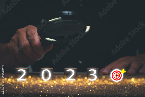New Year's Goal Planning Ideas 2023. Hand holding magnifying glass looking wooden block cube with 2023 new year goals icon, business plan and corporate vision.start new year, holidays and celebrations