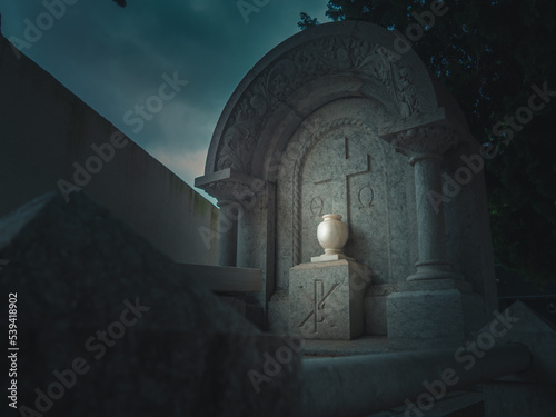 tomb in a Christian cemetery adorned with a carved floral design with an urn illuminated by a beam of light at night in Vandellòs, Catalonia, Spain