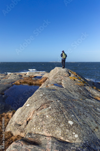 A caucasian man hiking on a rock by the sea with a backpack