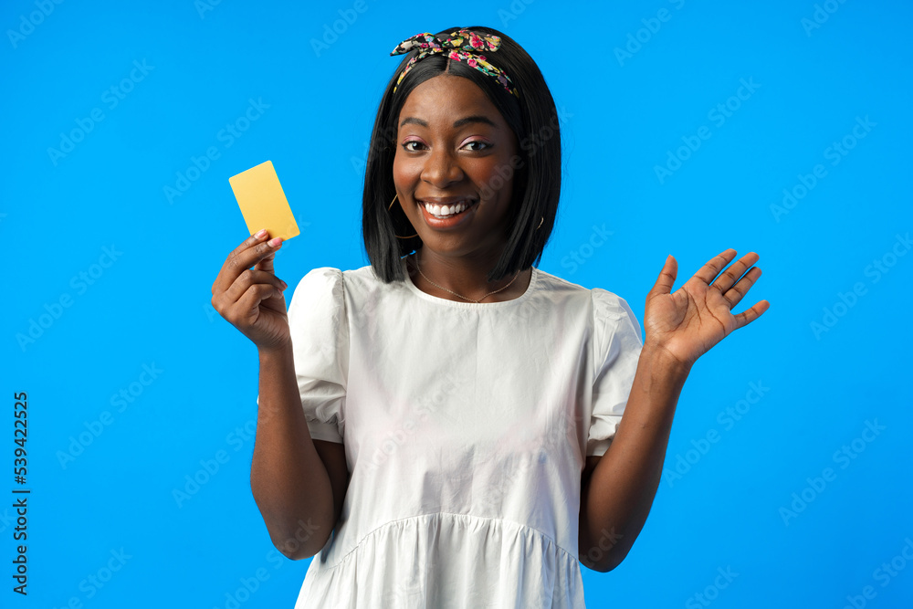 Young african woman holding credit card in hand against blue background Young african woman holding credit card in hand against blue background
