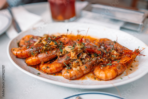 Traditional Spanish tapas. Aromatic delicious grilled king prawns with herbs and garlic pepper sauce on a white plate in a restaurant. Spanish cuisine dish. 