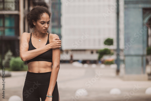 Curly-haired young female athlete suffering from pain in her shoulder