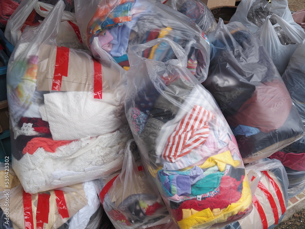 Lots of different colored used clothes packed in large plastic bags sealed with red scotch tape to donate to the poor or those affected by floods, fires, Concept of ​​sharing unused items with society