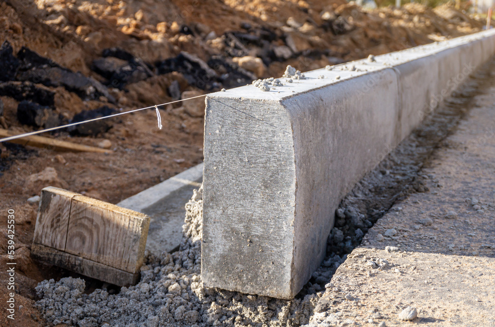 Concrete curbs installation works at road construction site. String line level guide. Close-up. Concrete curbs installation works at road construction site. String line level guide. Close-up.