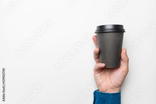 male hand with a paper black glass of coffee on a white background, close-up. mockup for banner