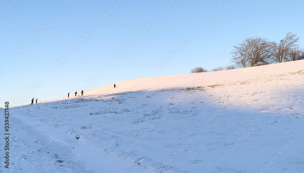 Danish winter landscape with white fields and hills and children sledging in the snow