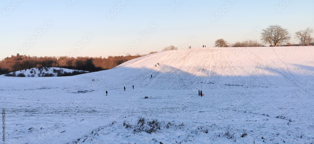 Danish winter landscape with white fields and hills and children sledging in the snow Danish winter landscape with white fields and hills and children sledging in the snow