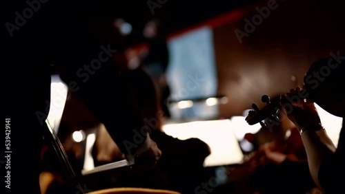 Violinist playing the violin close-up. The symphony orchestra plays the composition under the leadership of the conductor