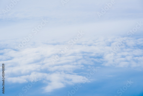 Flying Above the Clouds with Blue Skies in an Airplane Looking out of the Window. White fluffy clouds below with the darkness of space. Beautiful white clouds.