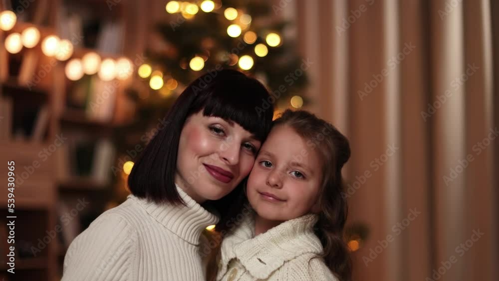 Close up video portrait of lovely family of two, beautiful young mother and her cute little daughter in warm knitted white sweaters in front of decorated Christmas tree. Close up video portrait of lovely family of two, beautiful young mother and her cute little daughter in warm knitted white sweaters in front of decorated Christmas tree.