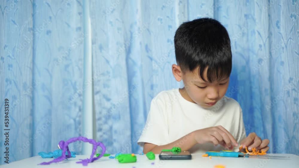 child playing with toys, an Asian boy Sitting and making dolls from plasticine on a white table in the house child playing with toys, an Asian boy Sitting and making dolls from plasticine on a white table in the house