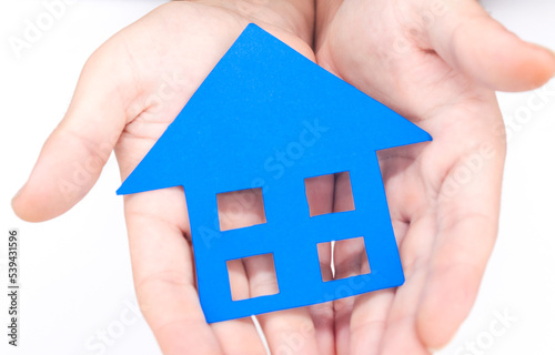  close up hands holding a blue paper house on white background. Concept of housing, buying and selling houses, rentals, real estate, mortgage