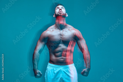 Powerful athletic man with muscular naked torso looks up in colorful studio light. Long exposure. Sport club advertising © Georgii