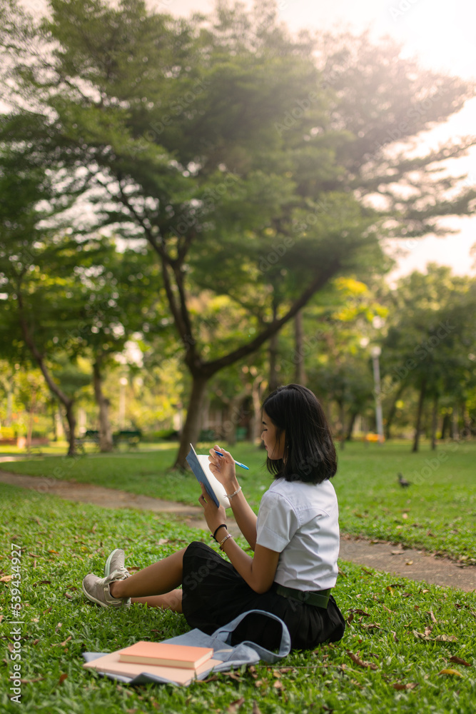 Beautiful portrait photo of a young beautiful asian female thai lady in university student uniform holding a book in a park Beautiful portrait photo of a young beautiful asian female thai lady in university student uniform holding a book in a park