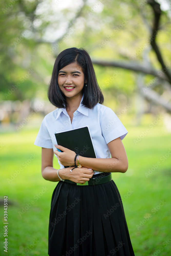 Beautiful portrait photo of a young beautiful asian female thai lady in university student uniform holding a book in a park Beautiful portrait photo of a young beautiful asian female thai lady in university student uniform holding a book in a park