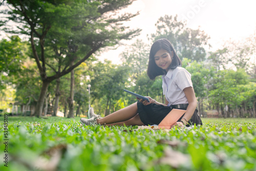 Beautiful portrait photo of a young beautiful asian female thai lady in university student uniform reading a book in a park