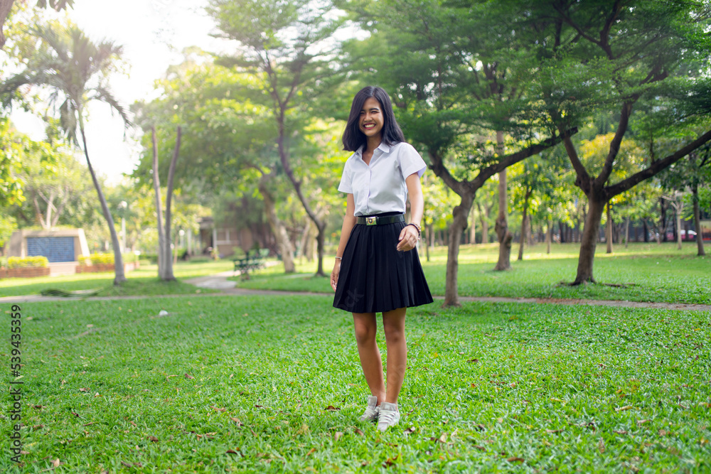 Portrait photo of a young asian beautiful female thai university student lady running happily and relaxingly in a park