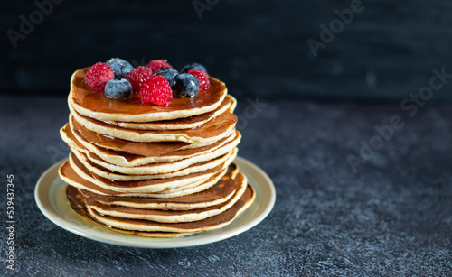 Pancakes with berries and honey on dark background with copy space