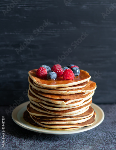 Pancakes with berrie and honey on dark background close-up, centered