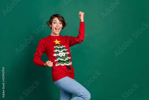 Photo of astonished lady stylish ugly jumper raise hand arm win lottery hooray yeah scream empty space isolated on green color background