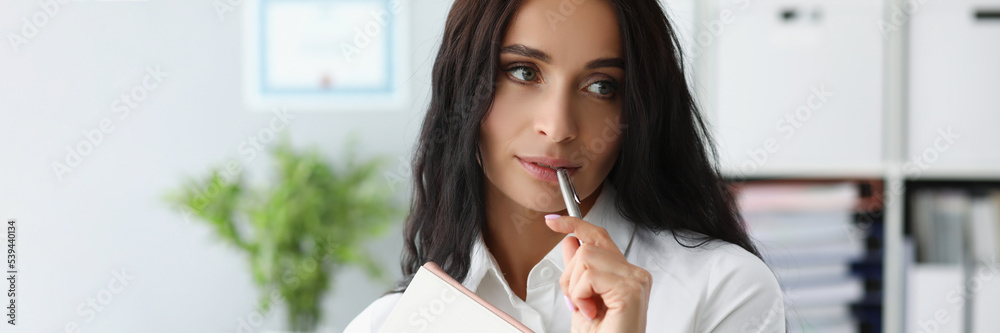 Woman holding silver pen on mouth, thinking about new ideas to journal Woman holding silver pen on mouth, thinking about new ideas to journal