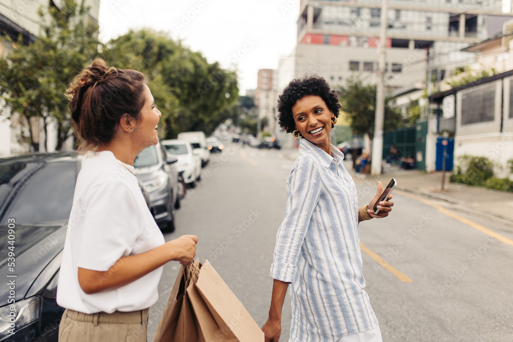 Happy young women crossing the street while shopping in the city