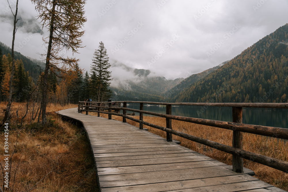 Wanderweg / Holzsteg am Antolzer See in den Dolomiten. Herbstliche Landschaft am See in Südtirol. Regnerisches Wetter