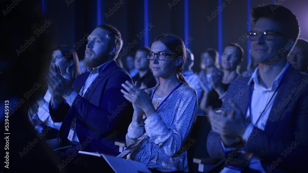 Young Woman Sitting in a Crowded Audience at a Business Conference. Female Attendee Cheering and Clapping After a Motivational Keynote Speech. Auditorium with Young Successful Businesspeople.