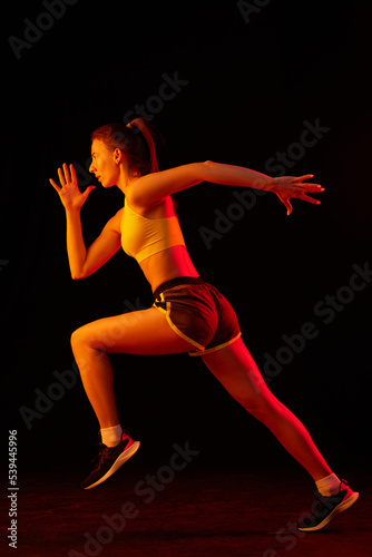 Running technique. Professional female jogger running isolated on dark background in neon light. Sport, fitness, speed and energy concept.