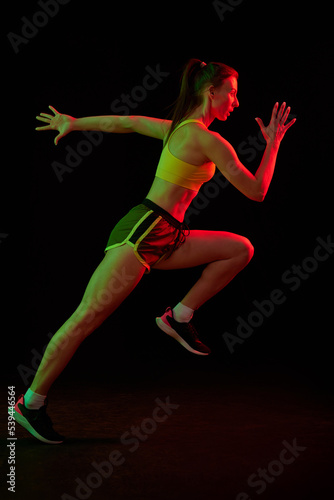 Professional female athlete running isolated on dark background in neon light. Healthy lifestyle, skills, sport, fitness, speed and energy concept. © master1305